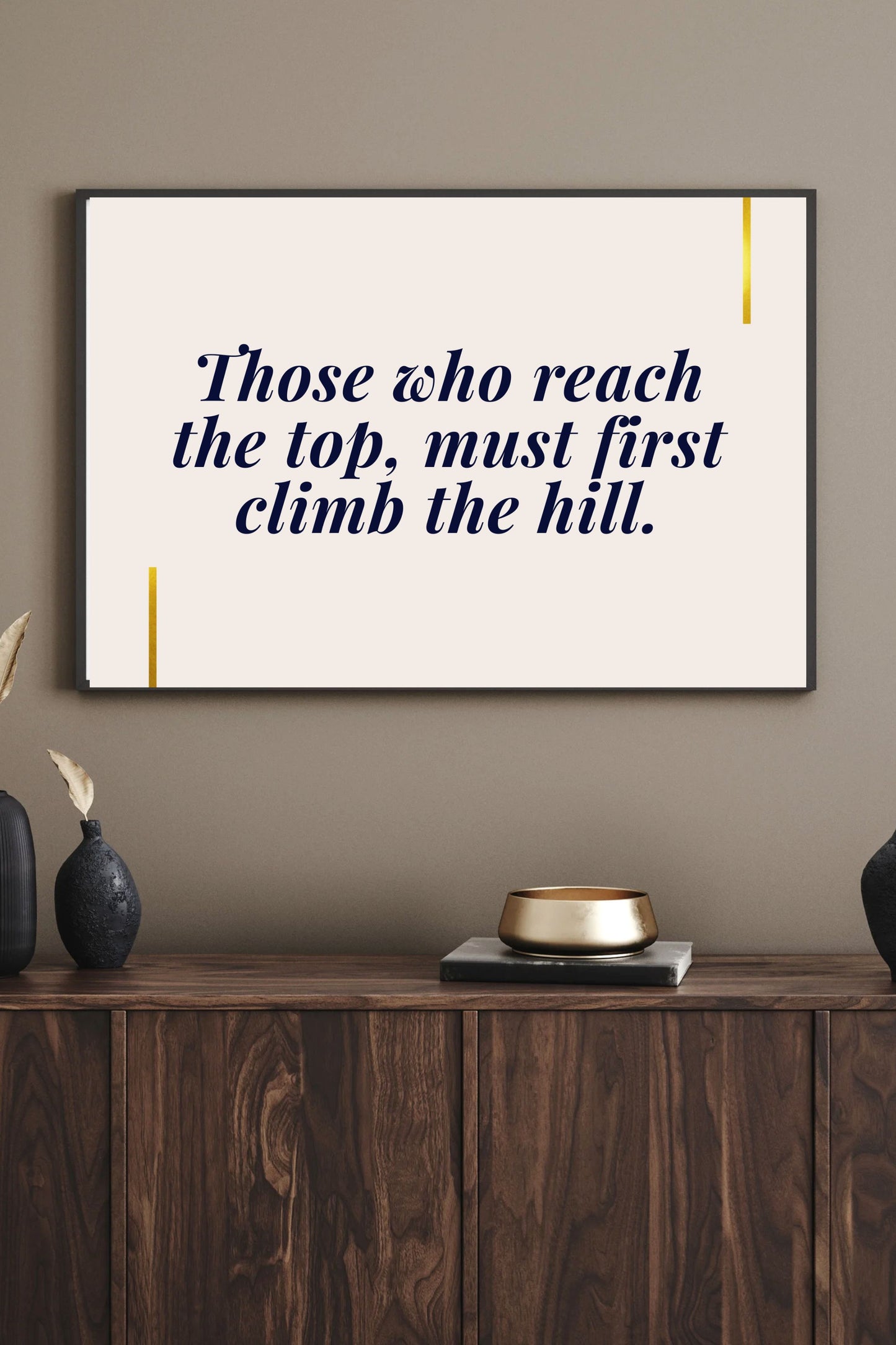 Motivational printable wall art featuring the quote "Those who reach the top, must first climb the hill" in navy serif font with gold accent lines, styled above a walnut sideboard with gold bowl, black vases, and a warm neutral wall—creating a refined, inspiring atmosphere.
