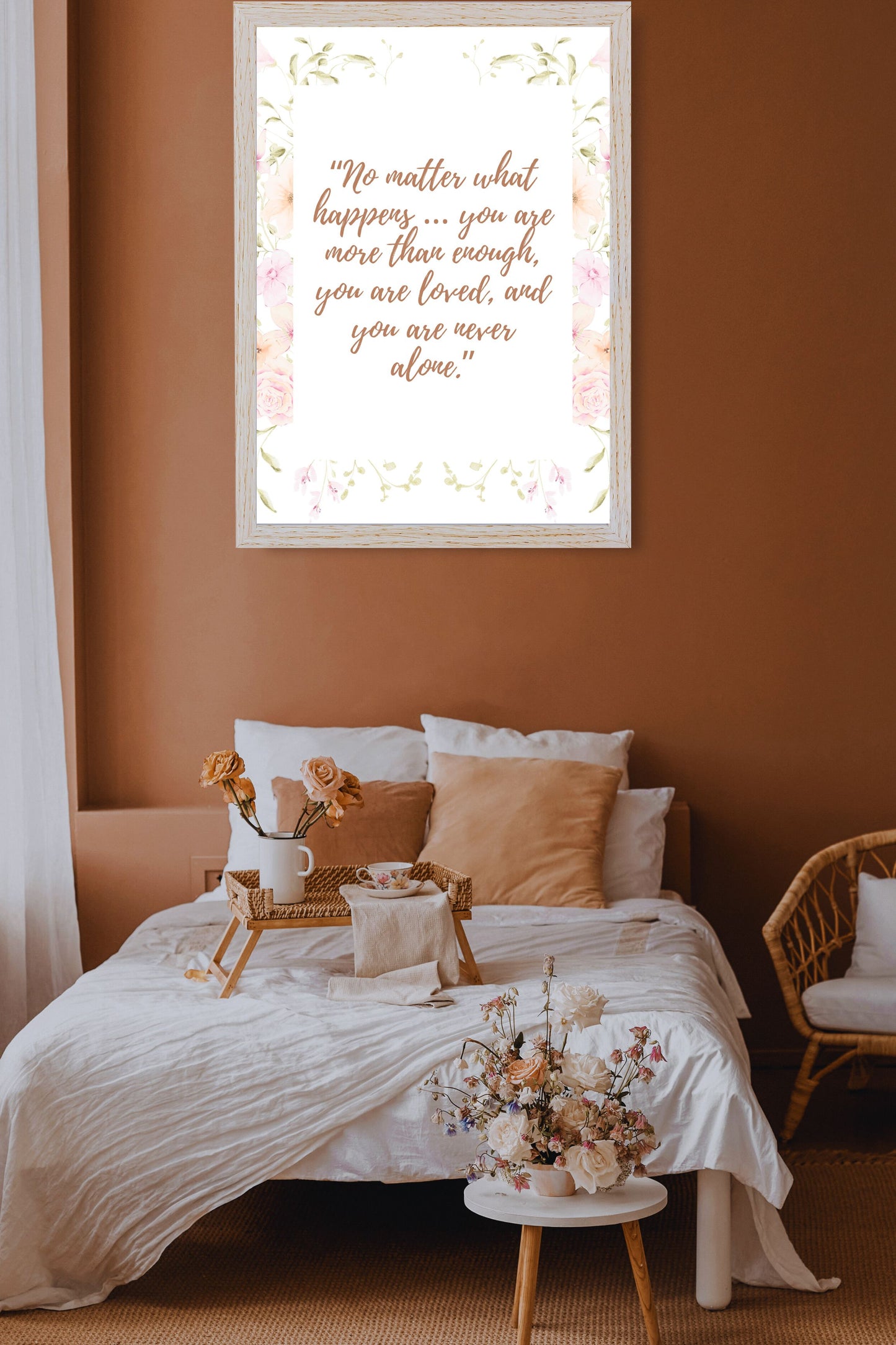 Motivational printable wall art featuring the quote "No matter what happens… you are more than enough, you are loved, and you are never alone" in elegant script with a pastel floral border, displayed above a cozy neutral bed with peach and ivory accents in a calm bedroom.