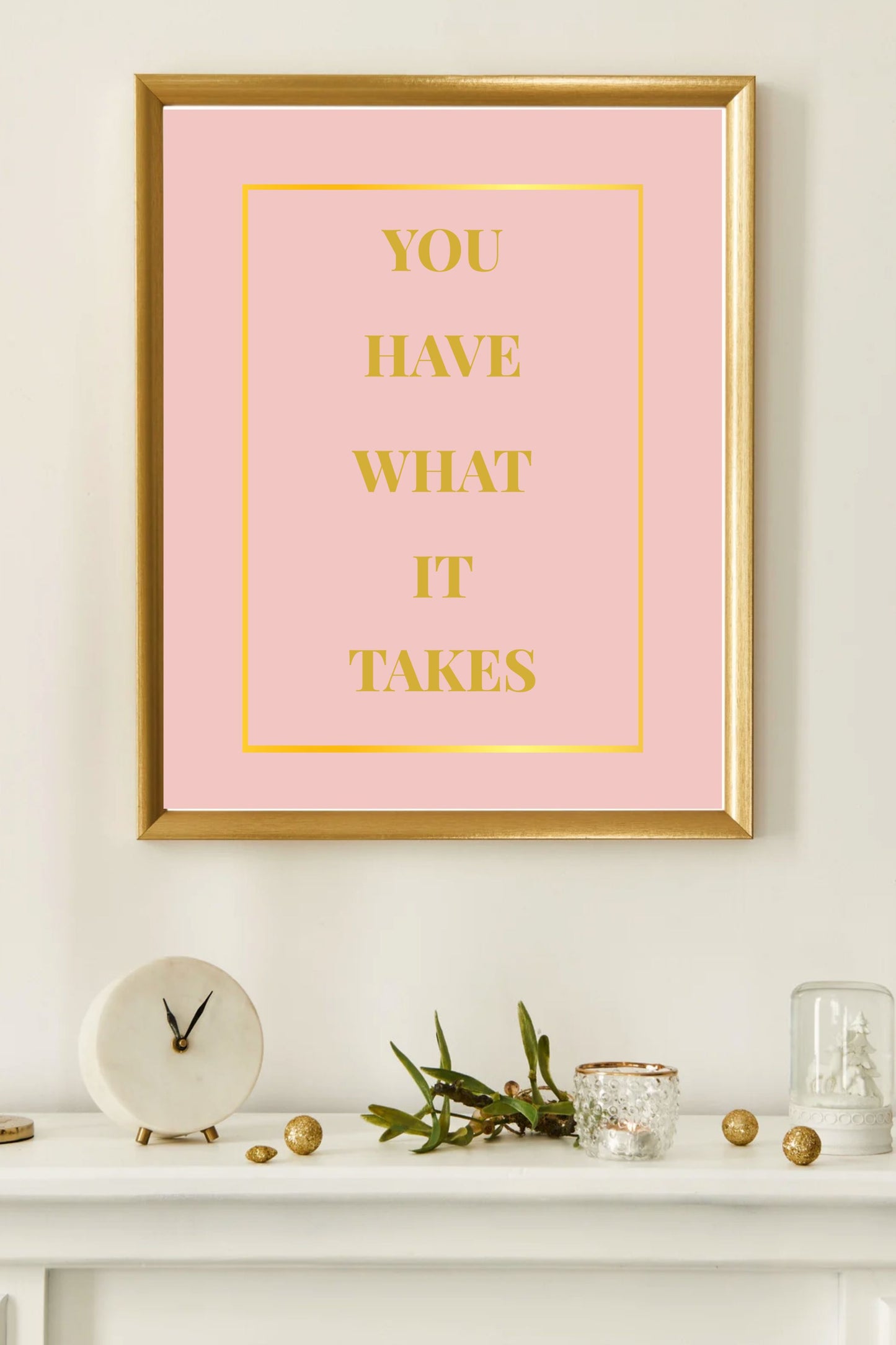 Motivational printable wall art featuring the quote "You Have What It Takes" in gold block letters on a blush pink background with a gold border, framed in gold and displayed on a white mantel with modern, neutral decor accents and a marble clock.