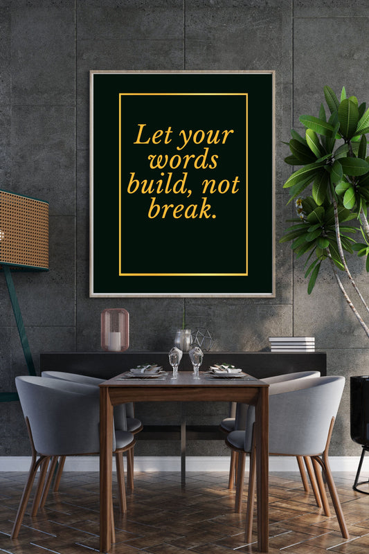 Motivational printable wall art featuring the quote "Let your words build, not break" in refined gold script, set within a gold border on a deep green background; displayed above a modern dining table with gray chairs and lush green plant, creating a calm, sophisticated atmosphere.