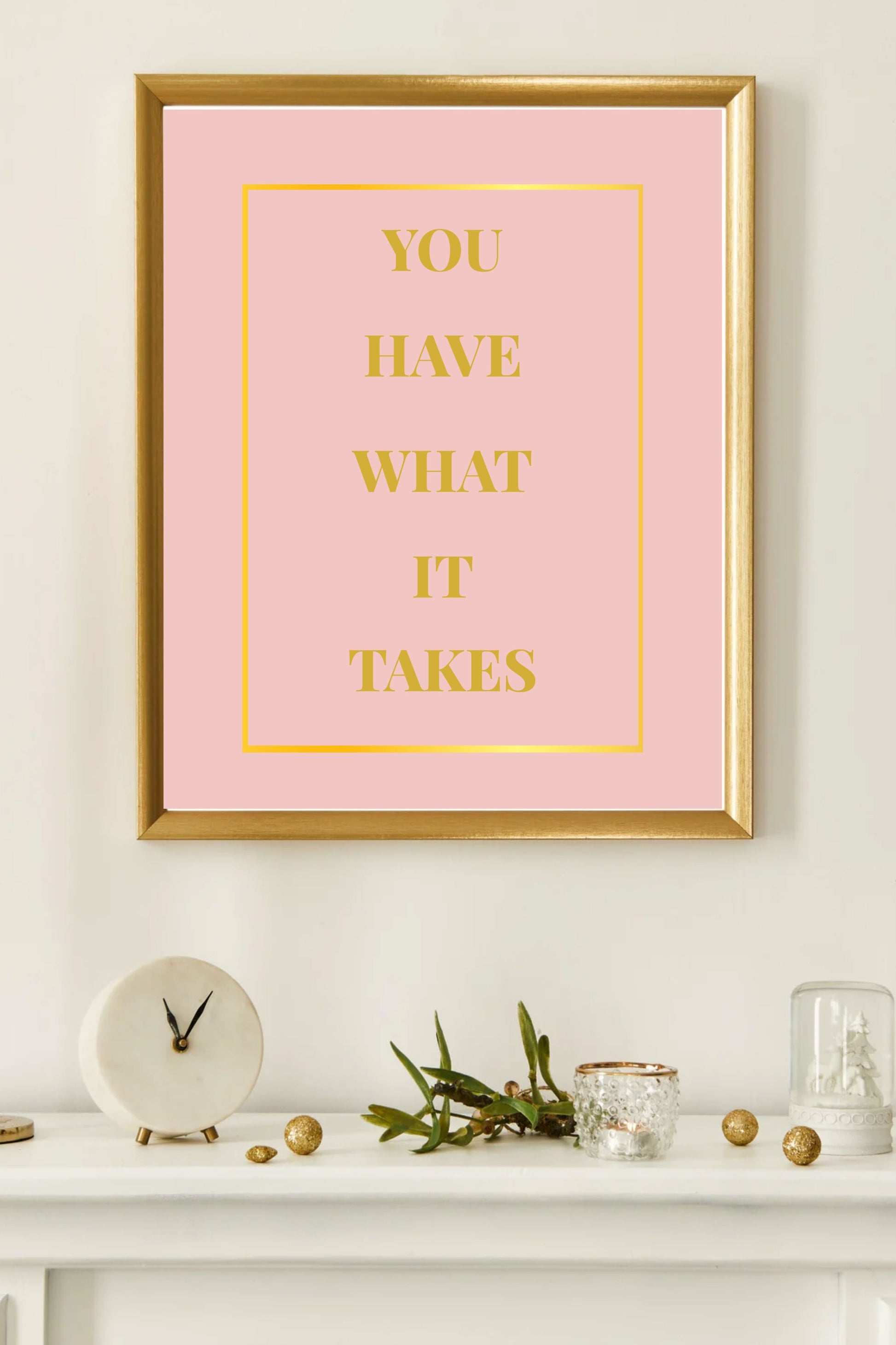 Motivational printable wall art featuring the quote "You Have What It Takes" in gold block letters on a blush pink background with a gold border, framed in gold and displayed on a white mantel with modern, neutral decor accents and a marble clock.
